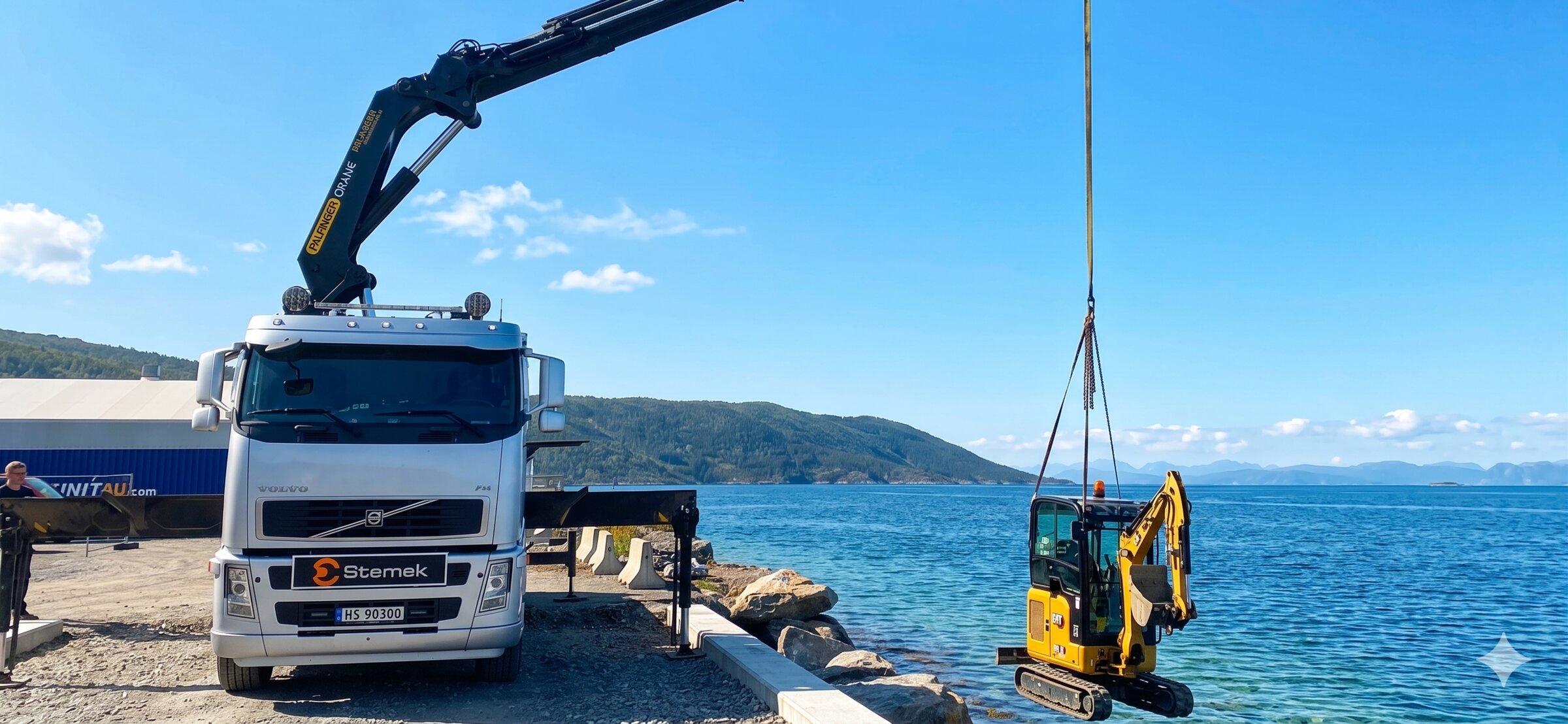 Stemek-merket Volvo-kranbil med Palfinger Hiab-kran løfter en CAT gravemaskin over fjorden